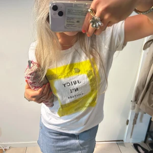 Vit Juicy Couture t-shirt med print - Vit t-shirt från Juicy Couture med coolt gult och glittrigt print framtill där det står 'JUICY N°1 COUTURE'. Den har lite fläckar vid ärmarna som jag försöker få med på den sista bilden. Men annars inga konstigheter! 