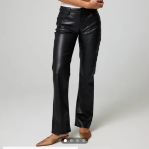 Svarta bootcut byxor i skinnimitation - Snygga svarta byxor i skinnimitation med bootcut-snitt och klassisk femficksdesign. Byxorna har normal passform och stängs med dragkedja och knapp. Perfekta för dig som vill ha en edgy och trendig look.