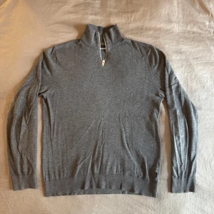 Grå half zip tröja Jack & Jones - Mörkgrå stickad tröja från Jack & Jones med half zip och hög krage. Tröjan har lång ärm, ribbade muddar och är i mjukt material. Enkel och stilren design som funkar till många outfits.