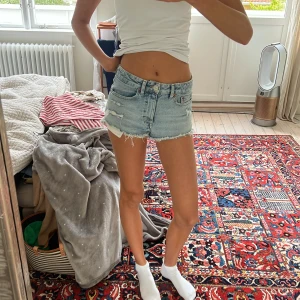 Ljusblå jeansshorts från Divided - Snygga ljusblå jeansshorts från Divided med råa, fransiga kanter och slitna detaljer. Klassisk femficksmodell med dragkedja och knapp. Perfekta för varma dagar och ger en avslappnad vibe till din outfit.