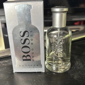 Hugo Boss Bottled Eau de Toilette 50ml - Snygg och stilren parfymflaska från Hugo Boss Bottled, 50ml. Flaskan är transparent med silverfärgat lock och BOSS-logga i relief. Doften har fräscha toppnoter av äpple, hjärtnoter av kanel och geranium samt basnoter av sensuella träslag. Perfekt för dig som gillar klassisk och modern stil.