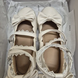 Vita klackskor med rosett och spets 37 - Supersöta vita klackskor med chunky låg klack, rund tå och dekorativa rosetter framtill. Skorna har flera remmar med fina spetsdetaljer och spännen. Använd en gång. 