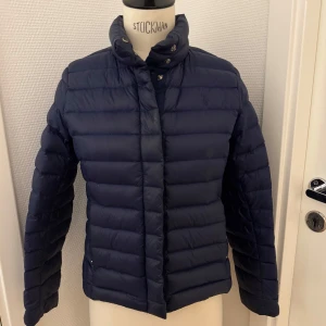 Blå dunjacka från Polo Ralph Lauren - Snygg mörkblå dunjacka från Polo Ralph Lauren med broderad logga på bröstet. Ca stl 12-14 år men hon som haft den är 15 år och brukar ha xs. Jackan knappar och dragkedja. Yttertyget är i nylon och fodret består av vitt ankdun för extra värme. Perfekt för kalla dagar. En liten lagning på jackan -därav priset. Lagningen syns inte alls faktiskt. Men på sista bilden har jag ljusat upp fotot så du kan se. Kan hämtas på Hägerstensåsen i Stockholm 🌸