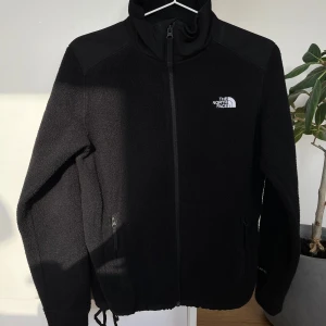 Svart fleecejacka från The North Face - Svart fleecejacka från The North Face med hög krage och hel dragkedja och två fickor med dragkedja.