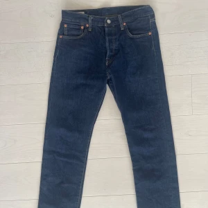 Levi's 501 mörkblå jeans W30 L30 - Klassiska Levi's 501 jeans i mörkblå tvätt med raka ben och fem fickor. Jeansen har knappgylf, kontrastsömmar och den ikoniska läderpatchen bak i midjan. Perfekt för dig som gillar tidlös stil och vill ha ett par jeans som funkar till allt.     Säljer pga att dem bar legat i garderoben och samlat damm, använts ca 4-8 ggr och har inget tecken på användning alls.     (Nypris: 1299kr)