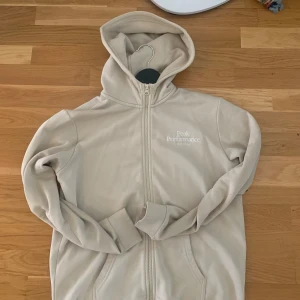 Beige hoodie från Peak Performance - Snygg beige hoodie från Peak Performance med dragkedja och huva. Tröjan har diskret logga på bröstet, långa ärmar och ribbade muddar. Perfekt för en chill och avslappnad stil. Gjord i mjukt material som känns skönt mot huden. Andvänd rätt mycke fast fortfarande i ganska okej skick
