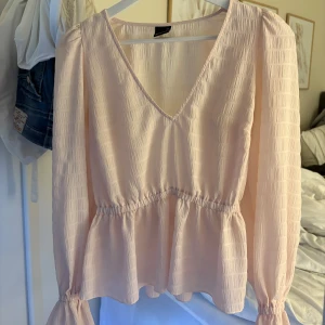 Ljusrosa blus från Gina Tricot XS - Supersöt ljusrosa blus från Gina Tricot i storlek XS. Blusen har v-ringning, långa ärmar med volangdetalj vid ärmslut och resår i midjan för en snygg siluett. Tunt, lätt material med diskret struktur som ger en romantisk vibe.