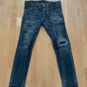 Dsquared2 slim jeans - Säljer ett par grå jeans från Dsquared2 i storlek 46. De har en cool, sliten look med flera snygga hål och slitningar framtill. Klassisk femficksmodell med smal passform och låg midja. Perfekta för dig som gillar streetstyle och vill sticka ut. Liknar Dondup i passform, passar runt 180. Finns en liten fläck på insidan, syns ej vid användning. självklart äkta.