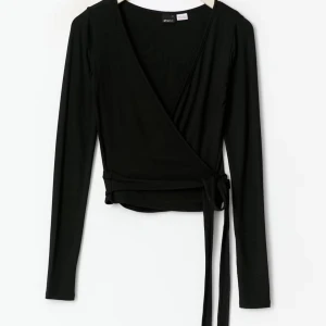 Svart omlottopp från Gina Tricot - Svart omlottopp med långa ärmar och knyt i midjan från Gina Tricot. Toppens omlottdesign ger en snygg v-ringning och den är tillverkad i mjuk bomullsmix som sitter skönt och följsamt på kroppen. Perfekt att styla med både jeans och kjol.