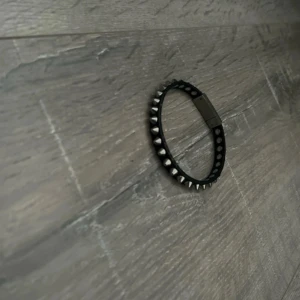 Svart armband med nitar - Coolt svart armband med silvriga nitar runt hela bandet. Perfekt för dig som gillar en edgy stil och vill sticka ut lite extra. Armbandet har ett smidigt spänne och passar både tjejer och killar. Snygg detalj till din outfit!