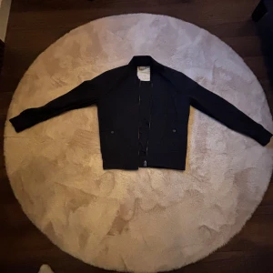 Svart bomberjacka från Esprit - Snygg svart bomberjacka från Esprit med klassisk krage och raka linjer. Jackan har dragkedja framtill, två fickor med knappstängning och ribbade muddar vid ärmar och nederkant. Perfekt för dig som gillar stilren och enkel design.