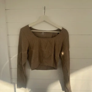 Beige ribbad croppad topp H&M - Säljer en beige ribbad croppad topp från H&M med lång ärm och bred, fyrkantig ringning. Toppen har en mjuk och stretchig känsla, perfekt att styla med höga jeans eller kjol. Enkel men trendig design som passar till många looks.