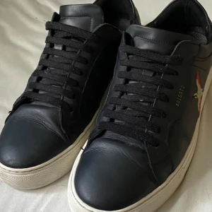 Svarta Axel Arigato sneakers i skinn - Ny pris 2700 ca. Snygga svarta sneakers från Axel Arigato i skinn med broderad fågel på sidan. Klassisk modell med svart snörning och vit platt sula. Perfekta för dig som gillar stilrena men ändå unika detaljer. Kommer med originalkartong.