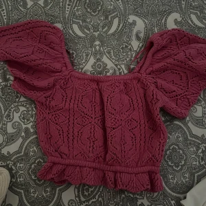 Rosa stickad croppad blus - Superfin rosa stickad blus med korta puffärmar och volangkant nertill. Snyggt hålmönster över hela toppen och offshoulder-modell som ger en trendig vibe. Perfekt för dig som vill sticka ut lite extra!
