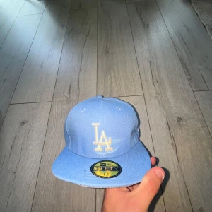 Ljusblå LA keps från New Era - Snygg ljusblå keps från New Era med LA-logga broderad framtill i vitt. Klassisk 59FIFTY-modell med platt skärm och ventilationhål. Perfekt för dig som gillar streetwear och sportig stil.