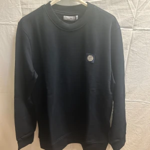 Marinblå sweatshirt från Stone Island - En stilren marinblå sweatshirt från Stone Island med klassisk rund hals och ikonisk logopatch på bröstet. Tröjan är i mjuk bomull och har långa ärmar samt ribbade muddar. Perfekt för dig som gillar clean streetwear med premiumkänsla.    