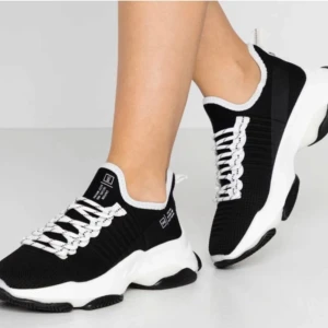 Steve Madden Svarta och vita sneakers med tjock sula - Säljer ett par svarta sneakers med vit och svart tjock sula. Skorna har stickad ovandel, vita snören med svarta detaljer och sportig design. Perfekta för en trendig och bekväm look.