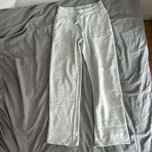 Ljusgrå mjukisbyxor med dragsko - Säljer ett par ljusgrå mjukisbyxor med resår och dragsko i midjan. Byxorna har raka ben och två fickor framtill. Perfekta för en avslappnad stil och superbekväma att ha på sig.
