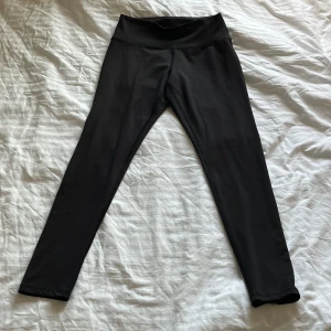 Svarta träningstights från H&M Move - Svarta tights med hög midja från H&M Move. Tillverkade i ett stretchigt syntetmaterial som passar perfekt för träning. Tightsen har en enkel och stilren design utan synliga detaljer eller mönster.