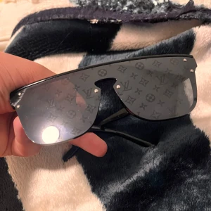 Svarta solglasögon  - Stilrena svarta solglasögon med monogrammönster på glasen. Modellen har en oversized, rektangulär form och tunna skalmar i svart. Perfekt accessoar för att lyfta din look.