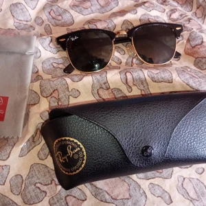 Svarta solglasögon från Ray-Ban - Klassiska svarta solglasögon från Ray-Ban med guldiga detaljer och rundade glas. Snygg retrostil med svart båge och Ray-Ban-logga på linsen. Kommer med originalfodral.