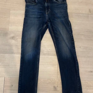 Mörkblå jeans från Replay - Snygga mörkblå jeans från Replay med klassisk femficksdesign och kontrastsömmar. Jeansen har raka ben och subtila slitningar framtill för en cool look. Perfekta för dig som gillar en tidlös stil med lite edge.