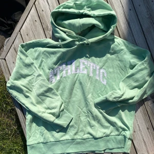 Mintgrön hoodie med ATHLETIC-tryck - Säljer en mintgrön hoodie med vit ATHLETIC-text på bröstet. Tröjan har huva med dragsko och långa ärmar med muddar. Perfekt för en avslappnad stil och supermjuk insida.