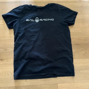 Svart t-shirt från Sail Racing - Säljer en svart t-shirt från Sail Racing med vit logga tryckt på bröstet. Klassisk passform och rund halsringning. Perfekt för en avslappnad stil och enkel att matcha med andra plagg. Står large men den är mer medium eller S passande