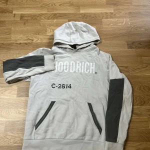 Beige och grå HOODRICH hoodie - hoodie och byxor från HOODRICH i gråa detaljer på ärmar och ficka. Stor vit logga framtill och världskarta tryckt. Perfekt för dig som gillar tracksuits och vill sticka ut.
