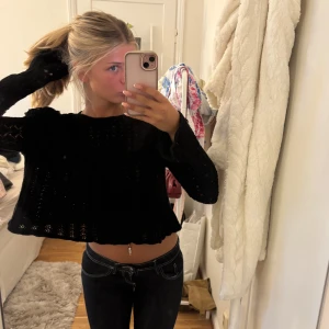 Svart stickad croppad tröja - Svart stickad tröja med croppad passform och vida, långa ärmar. Tröjan har ett genombrutet mönster och volangdetaljer vid axlarna. Perfekt för dig som gillar en lite mer unik och trendig look.