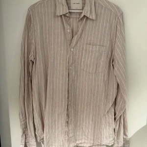 Beige randig linneskjorta A Day's March - Snygg beige skjorta i linne från A Day's March med vita vertikala ränder. Klassisk krage, bröstficka och knäppning framtill. Perfekt för en avslappnad men stilren look. Långärmad och luftig modell.