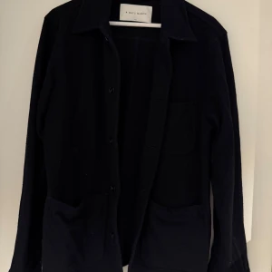 Svart/mörkblå overshirt från A Day's March - Stilren svart/mörkblå overshirt från A Day's March med klassisk krage, knäppning framtill och stora fickor. Perfekt lager-på-lager-plagg med lång ärm och enkel design som funkar till allt. Materialet känns mjukt och håller värmen.