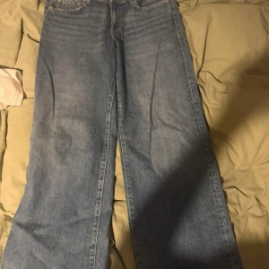 Blå wide jeans från Gina Tricot - Säljer ett par klassiska blå jeans från Gina Tricot med breda ben och normal passform. Jeansen har fem fickor, knapp och dragkedja framtill samt bälteshällor. Perfekta för en avslappnad och trendig look.
