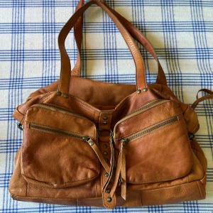 Brun skinn axelväska med dragkedjor - Säljer en vintage brun axelväska, miumiu lookalike i äkta skinn med två stora framfickor med dragkedjor. Väskan har dubbla handtag och en rymlig insida. Lädret är supermjukt. Band för crossbody tillkommer.