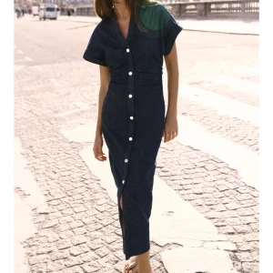 Marinblå jeansklänning med knappar - Snygg marinblå jeansklänning med korta ärmar och knappar längs hela framsidan. Klänningen har en slits framtill och markerad midja för en smickrande passform. Perfekt för dig som gillar en stilren och trendig look. Klänningen är helt ny med prislapp! 