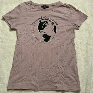 Ljuslila tröja stl 146-152 - En ljuslila t-shirt med tryck av en jordglob och texten *"The world is ours to save"*. Kortärmad, i mjukt tyg och med ett miljöinspirerat budskap.