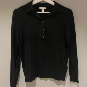 Svart långärmad pikétröja - Klassisk svart pikétröja från H&M med lång ärm och knappar framtill. Tröjan har en stilren krage och är gjord i mjukt bomullsmaterial. Perfekt för en clean och enkel look.