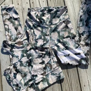 Camo-mönstrade träningstights och topp från Stronger - Säljer ett par camo-mönstrade träningstights från Stronger i gröna och beige toner. Tightsen har hög midja och vita detaljer på ena benet. Även en matchande sport topp/ sport bh. Perfekta för gymmet eller löprundan.