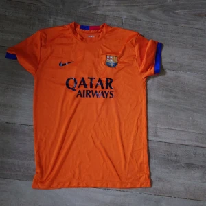 Barça Messi 10 orange fotbollströja Nike - Snygg orange FC Barcelona fotbollströja med Messi 10-tryck på ryggen och Qatar Airways-logga på bröstet. Tröjan har korta ärmar med blå och röda detaljer och klubbmärke på bröstet. Perfekt för dig som älskar fotboll och Messi.