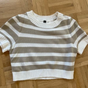Randig stickad tröja H&M - Superfin croppad stickad tröja från H&M med beige och vita ränder. Tröjan har korta ärmar, rund halsringning och ribbade kanter. Färgen är mer beige och ljus i verkligheten än på bild. 