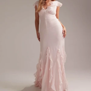 Ljusrosa maxiklänning med volangdetaljer - En ljusrosa maxiklänning med volanger längs axlar och kjol. Klänningen är aldrig använd och har prislapp kvar. Klänningen har v-ringning både fram och bak och formar kroppen på ett fint sätt. Perfekt för speciella tillfällen som bal och bröllop. 