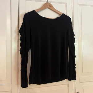 Långärmad tröja/blus - Svart långärmad tröja/blus med snygga volangdetaljer längs ärmarna. 