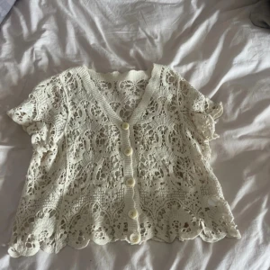 Vit spetsblus med knappar - Superfin vit blus i spets med korta ärmar och v-ringning. Blusen har dekorativa knappar framtill och ett vackert virkat mönster över hela plagget. Perfekt för dig som gillar romantisk och bohemisk stil. Köpt i Grekland💕