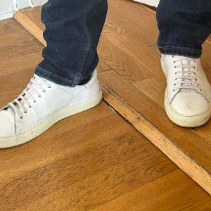 Vita sneakers från Axel Arigato - Säljer ett par stilrena vita sneakers från Axel Arigato med klassisk design och låga skaft. Skorna har snörning och platt sula, perfekta till jeans eller andra vardagsoutfits.