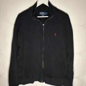 Ralph Lauren zip - Svart ziptröja från Polo Ralph Lauren i storlek XL. Klassisk modell med röd logga, sparsamt använd och i bra skick. Ingen luva klädd modell.