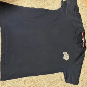 Mörkblå Moncler t-shirt med logga - Snygg mörkblå t-shirt från Moncler i bomull med klassisk rund hals och broderad logga på bröstet. Enkel och stilren design med korta ärmar och diskret röd-vit detalj i nacken. Perfekt för dig som gillar exklusiva basics.