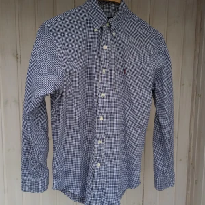 Rutig blåvit skjorta Polo Ralph Lauren - Snygg blåvit rutig skjorta från Polo Ralph Lauren i slim fit-modell. Skjortan har klassisk krage, knappar framtill och långa ärmar. Tillverkad i stretchig bomull för extra komfort. Perfekt för dig som gillar stilren och tidlös look. blå/ vit rutig.
