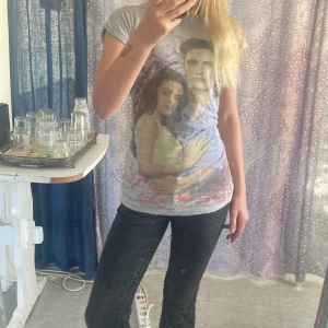 Twilight Breaking Dawn t-shirt grå - Grå t-shirt med tryck från Twilight Breaking Dawn. Motiv med karaktärer och dekorativa lila och röda detaljer. Klassisk rund hals och korta ärmar. Perfekt för dig som älskar Twilight och vill ha något unikt i garderoben.