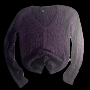 Lila kabelstickad tröja Ralph Lauren - Snygg kabelstickad tröja från Ralph Lauren Sport i en djup lila färg. Tröjan har v-ringning, lång ärm och är gjord i 100% bomull. Perfekt för dig som gillar klassisk stil med en twist. Passar till både jeans och kjol.