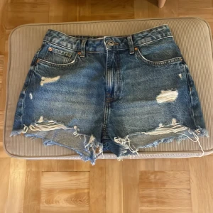Blå slitna jeansshorts från Primark - Snygga blå jeansshorts från Primark med slitna detaljer och fransig kant. Klassisk femficksmodell med hög midja och råa kanter för en cool, avslappnad vibe. Perfekta för sommardagar när du vill ha en chill och trendig look.